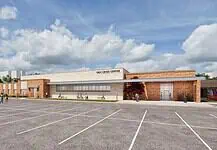 PRESS RELEASE: Plans for MAPS 4 Mental Health Crisis Center approved Exterior view of the OKC Crisis Center with a brick and tan facade and a spacious parking lot in the foreground, daytime with people walking nearby.