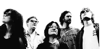 Five-person rock band standing side by side, looking up, in a black-and-white photo.