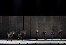 OKC Ballet presents a night of fierce dance, fresh stories with ‘SHORTS’ Line of dancers in black suits on a dim stage, with motion blur from moving bodies behind them.