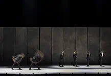 OKC Ballet presents a night of fierce dance, fresh stories with ‘SHORTS’ Line of dancers in black suits on a dim stage, with motion blur from moving bodies behind them.