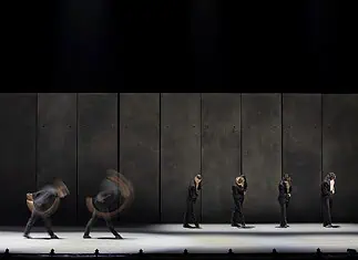 OKC Ballet presents a night of fierce dance, fresh stories with ‘SHORTS’ Line of dancers in black suits on a dim stage, with motion blur from moving bodies behind them.