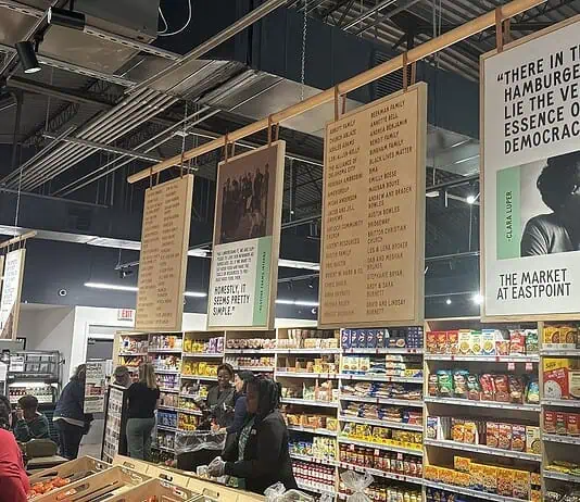 Market at EastPoint marks 5 years amid tough economy, Homeland plans Interior of a grocery or market with hanging posters above long aisles and shoppers browsing shelves of packaged foods.