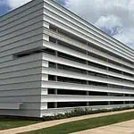 City Council’s data center exemptions raise questions of favoritism Modern white building with horizontal slat facade and a glass entrance, surrounded by a grassy lawn under a blue sky.