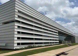 City Council’s data center exemptions raise questions of favoritism Modern white building with horizontal slat facade and a glass entrance, surrounded by a grassy lawn under a blue sky.