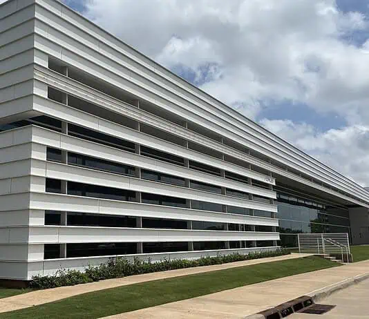 City Council’s data center exemptions raise questions of favoritism Modern white building with horizontal slat facade and a glass entrance, surrounded by a grassy lawn under a blue sky.