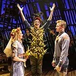 Country comedy ‘Shucked’ a corn-fed good time at Civic Center Actor in a leafy, harvest-themed costume raises arms on stage as four costumed performers look on with smiles on a wooden theater set.