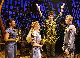 Country comedy ‘Shucked’ a corn-fed good time at Civic Center Actor in a leafy, harvest-themed costume raises arms on stage as four costumed performers look on with smiles on a wooden theater set.