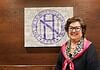Smiling woman in a black top with a pink scarf stands beside a wall featuring a large circular purple Nichols Hills logo.