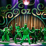 ‘The Wiz’ a magical, musical, cultural celebration at Civic Center Stage with neon-green 1920s signage and palm-leaf motifs; a group of dancers in green costumes perform a choreographed routine.