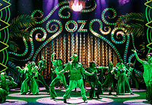 Stage with neon-green 1920s signage and palm-leaf motifs; a group of dancers in green costumes perform a choreographed routine.