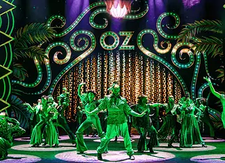 ‘The Wiz’ a magical, musical, cultural celebration at Civic Center Stage with neon-green 1920s signage and palm-leaf motifs; a group of dancers in green costumes perform a choreographed routine.