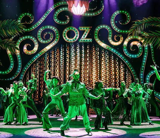 ‘The Wiz’ a magical, musical, cultural celebration at Civic Center Stage with neon-green 1920s signage and palm-leaf motifs; a group of dancers in green costumes perform a choreographed routine.