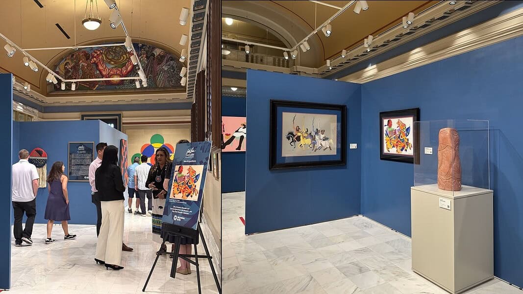 Museum gallery with blue walls, visitors viewing colorful artworks and a pink sculpture in a glass display case on a pedestal.