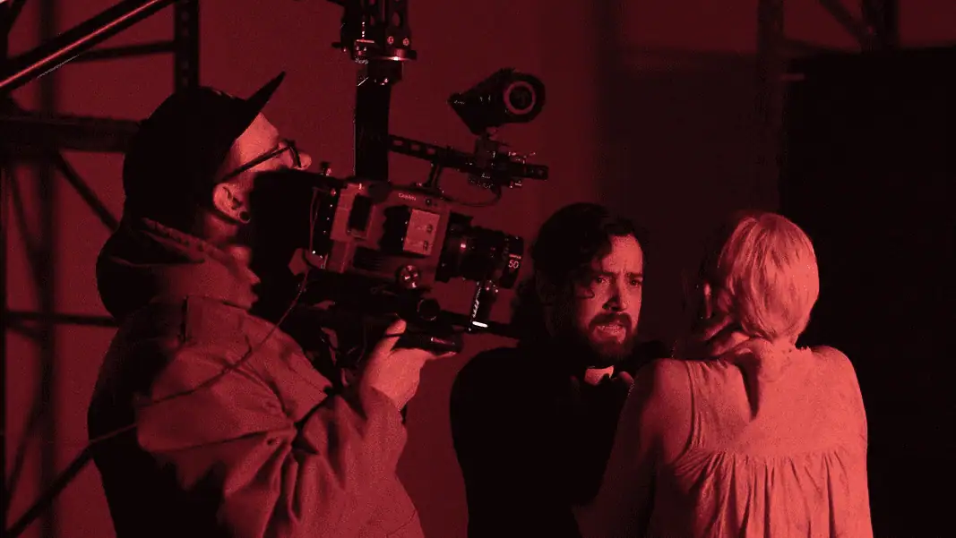 Absolution cropped Cameraman operating a large professional camera while a man and woman converse in a red-lit studio space.