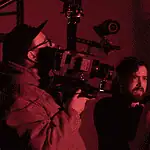 deadCenter shorts shine light on humanity, redemption, imagination Cameraman operating a large professional camera while a man and woman converse in a red-lit studio space.
