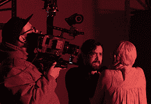 deadCenter shorts shine light on humanity, redemption, imagination Cameraman operating a large professional camera while a man and woman converse in a red-lit studio space.
