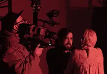 deadCenter shorts shine light on humanity, redemption, imagination Cameraman operating a large professional camera while a man and woman converse in a red-lit studio space.