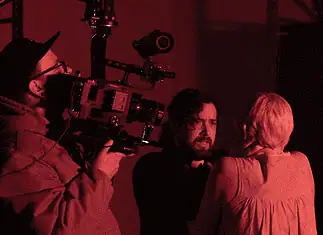 deadCenter shorts shine light on humanity, redemption, imagination Cameraman operating a large professional camera while a man and woman converse in a red-lit studio space.