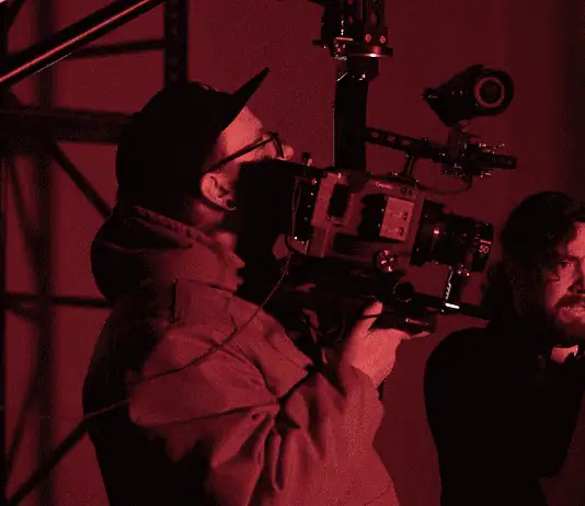 deadCenter shorts shine light on humanity, redemption, imagination Cameraman operating a large professional camera while a man and woman converse in a red-lit studio space.