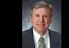 PRESS RELEASE: Former Oklahoma City Mayor Guy Liebmann passes away Professional head-and-shoulders portrait of a smiling middle-aged man in a dark suit and patterned tie against a muted blue-gray background.