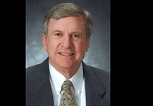 PRESS RELEASE: Former Oklahoma City Mayor Guy Liebmann passes away Professional head-and-shoulders portrait of a smiling middle-aged man in a dark suit and patterned tie against a muted blue-gray background.