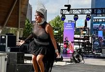 Drag performer wearing a tall silver crown and black sequined outfit performing on an outdoor stage at the Two Spirit Festival