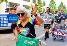 Oklahoma Pride Alliance looks beyond Pride Month Older woman with white hair in a rainbow shirt and sunglasses waves at a Pride parade, holding a green campaign sign for Cyndi Munson for Governor.