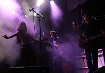 Crank up the summer with these hard-driving rock and metal shows Live music performance on a foggy stage with purple lighting; female singer left, keyboardist center, guitarist right.