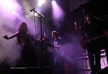 Crank up the summer with these hard-driving rock and metal shows Live music performance on a foggy stage with purple lighting; female singer left, keyboardist center, guitarist right.