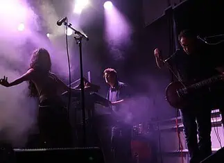 Crank up the summer with these hard-driving rock and metal shows Live music performance on a foggy stage with purple lighting; female singer left, keyboardist center, guitarist right.