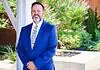 PRESS RELEASE: Metro Tech names Jeremy Cowley as new Deputy Superintendent Smiling man in a blue suit standing outdoors beside a brick column and greenery.