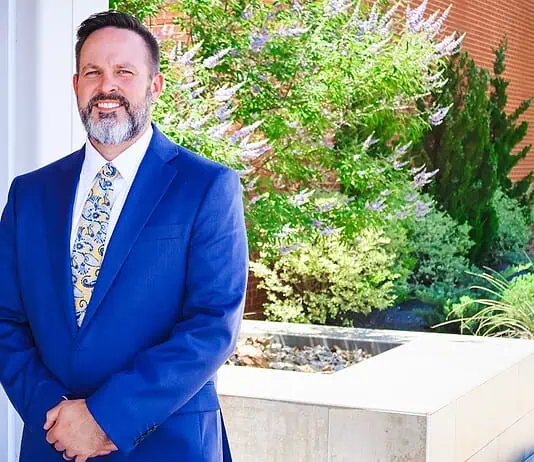 PRESS RELEASE: Metro Tech names Jeremy Cowley as new Deputy Superintendent Smiling man in a blue suit standing outdoors beside a brick column and greenery.