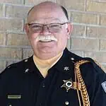 PRESS RELEASE: Francis Tuttle instructor named regional Teacher of the Year Older male sheriff in uniform smiling against a brick wall, with gold braid and badge.