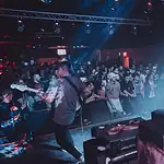 Showcases, mini-fests lift energy, noise, next generation of OKC music Band performs on stage in a crowded club, guitarist at left, drummer on the right, blue and red stage lights illuminating the audience.