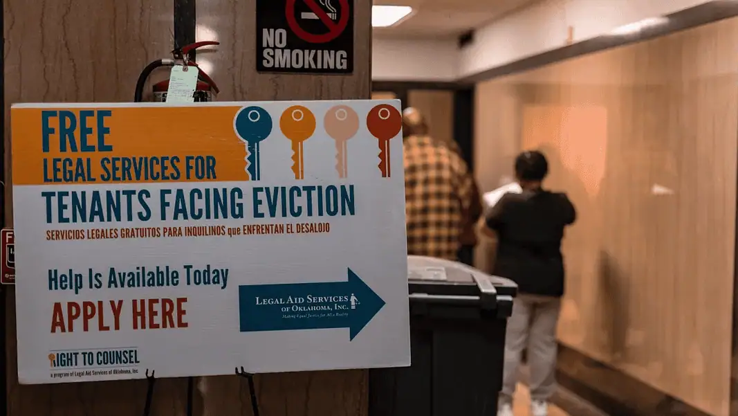 OK Watch evictions Poster offering free legal services for tenants facing eviction in a hallway; no smoking sign above and people in the background.