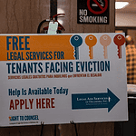 Poster offering free legal services for tenants facing eviction in a hallway; no smoking sign above and people in the background.