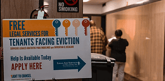 Poster offering free legal services for tenants facing eviction in a hallway; no smoking sign above and people in the background.