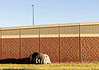 A small tent covered with a tarp tucked against a long brick wall on a sunny day, with a grassy foreground.