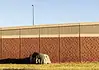 Three Cities, Three Approaches: How Oklahoma’s Homeless Encampment Sweeps Played Out Differently A small tent covered with a tarp tucked against a long brick wall on a sunny day, with a grassy foreground.