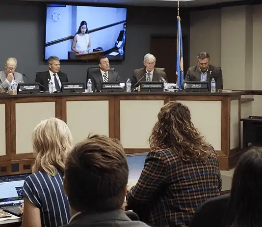 Oklahoma Turnpike Authority seeks $1.5B in bonds for construction costs Panel of officials seated at a curved dais in a government hearing room, seal on the wall and large screens showing a speaker behind them, audience in foreground.
