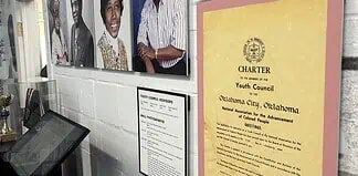 Wall exhibit with four large portraits of diverse adults, plus a yellow CHARTER poster labeled 'Youth Council' on a pink mat, and a framed council advisory list nearby, in a museum-like setting.