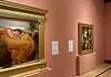 OKCMOA welcomes breadth, beauty of art from famed Puerto Rican museum Large ornate gold-framed painting on a pink wall, depicting a woman in an orange dress resting; to its right, a smaller framed religious-style artwork on a pedestal, also on pink wall.