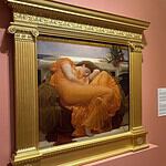 OKCMOA welcomes breadth, beauty of art from famed Puerto Rican museum Large ornate gold-framed painting on a pink wall, depicting a woman in an orange dress resting; to its right, a smaller framed religious-style artwork on a pedestal, also on pink wall.