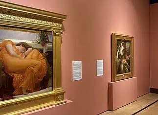 OKCMOA welcomes breadth, beauty of art from famed Puerto Rican museum Large ornate gold-framed painting on a pink wall, depicting a woman in an orange dress resting; to its right, a smaller framed religious-style artwork on a pedestal, also on pink wall.