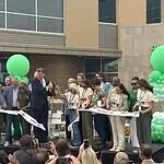 City, nonprofit, service leaders cut ribbon on new Diversion Hub Group of people on a stage cutting a white ribbon at a grand opening, with green balloons behind them.