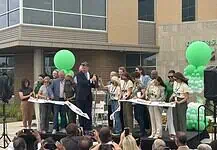 City, nonprofit, service leaders cut ribbon on new Diversion Hub Group of people on a stage cutting a white ribbon at a grand opening, with green balloons behind them.