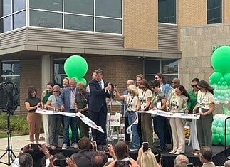 City, nonprofit, service leaders cut ribbon on new Diversion Hub Group of people on a stage cutting a white ribbon at a grand opening, with green balloons behind them.