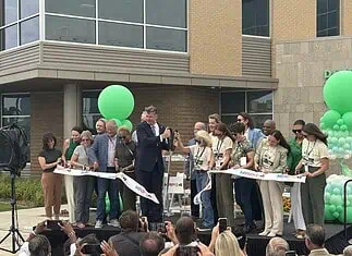 City, nonprofit, service leaders cut ribbon on new Diversion Hub Group of people on a stage cutting a white ribbon at a grand opening, with green balloons behind them.