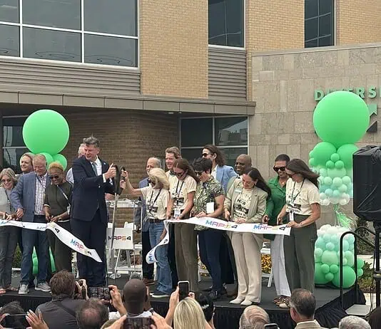 City, nonprofit, service leaders cut ribbon on new Diversion Hub Group of people on a stage cutting a white ribbon at a grand opening, with green balloons behind them.