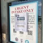 A door with a large posting labeled 'URGENT INTAKE ONLY' and a smaller 'NOTICE' sign attached over the poster.